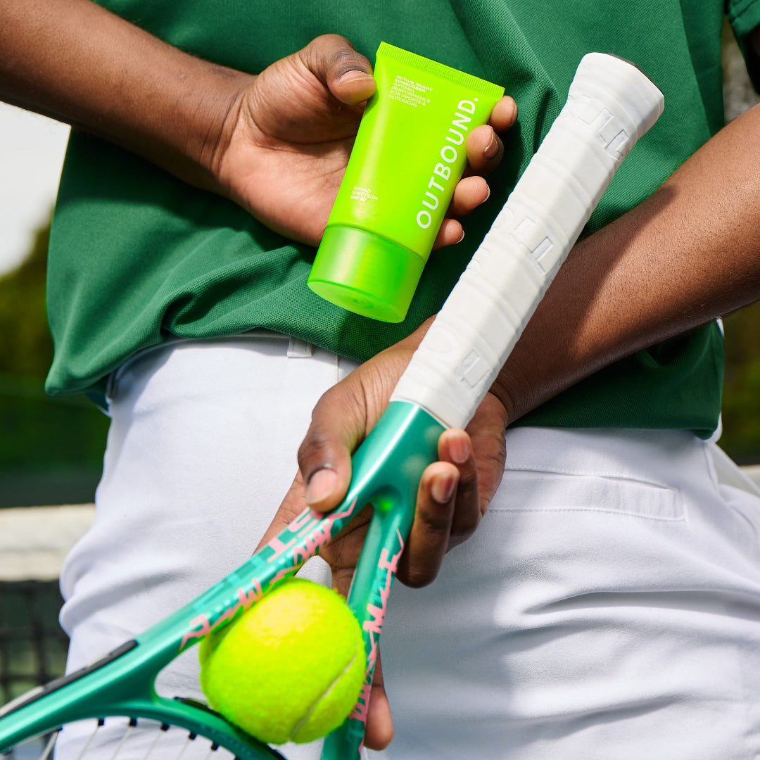 Tennis player holding a tennis racket, ball, and green sunscreen bottle with 'Outbound' branding.